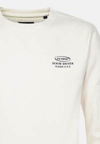 Light cream sweatshirt with a round neckline, featuring black printed text: "PETROL DENIM DRIVEN ALASKA U.S.A." on the front. Soft texture.