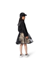 Μαύρο μπουφάν bomber με ριγέ μοτίβο και λογότυπο με γραφικά, φούστα από στρώσεις τούλι με λουλουδάτο σχέδιο, και λευκά αθλητικά παπούτσια με μαύρες φιόγκο λεπτομέρειες.