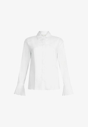 Blouse blanche à manches longues avec un col classique, un plastron devant et des manches cloche plissées. Confectionnée en tissu lisse et léger.