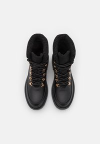 Bottines en cuir noir avec une doublure en polaire noire texturée, œillets en métal doré et lacets ronds. Bout arrondi et semelle durable.