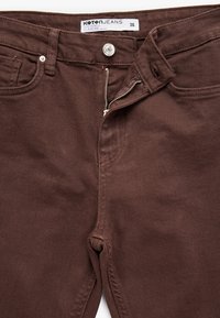 Ruusunväriset farkut, joissa on vetoketju ja nappisulku, flaerattu malli, viisi taskua ja ompeluyksityiskohtia. Hintalapussa lukee "Koton Jeans 36."