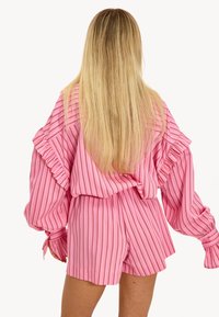 Blouse rayée rose avec des manches volantes associée à un short assorti. Fabriquée en tissu léger, elle présente des rayures verticales de largeurs variées.