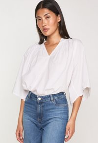 Top bianco, morbido e ampio con scollatura a V e collo arricciato, abbinato a jeans in denim blu a vita alta.