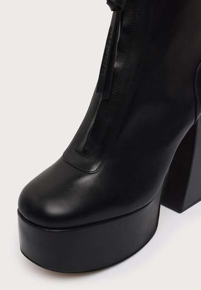 Botte plateforme noire avec talon haut bloc, bout arrondi, finition cuir lisse et détails de couture verticale. Aucun autre objet visible.