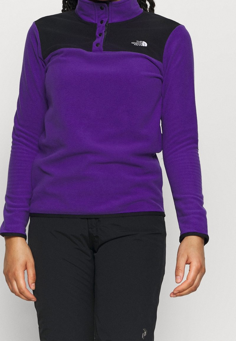 Paarse fleece top met zwarte schouderpanelen, halve knoopsluiting bij de kraag en lange mouwen. Voorzien van een logo op de linkerborst. Geweven stof.
