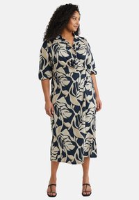 Patroonjurk met een marineblauwe basis en grote cr�èmekleurige bladvormen, kraaghals, korte mouwen en een getailleerde taille.