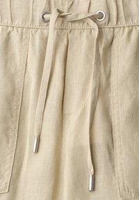 Pantalon en lin beige avec poches avant, taille élastique et cordons avec embouts métalliques argentés.