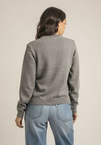 Pull en maille gris avec un col rond, des poignets et une ceinture côtelés, associé à un jean bleu clair. Texture lisse et design décontracté.