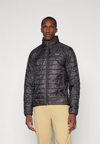 Veste isolante noire avec un design matelassé, col haut, fermeture éclair à l'avant et poches latérales. Fabriquée en matériau lisse et résistant à l'eau.