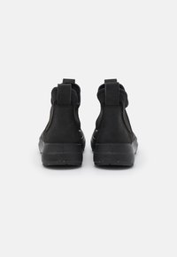 Bottes noires à cheville en suede et en matériau synthétique, dotées d'une texture lisse, d'une forme arrondie et d'une semelle robuste avec des accents sur le talon.