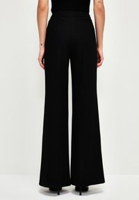 Zwarte, wijde broek met hoge taille. Glad, rekbaar stof. Geen zichtbare patronen of accenten. De zoom eindigt op enkelhoogte.