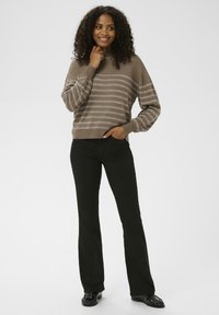 Pull marron à rayures avec une coupe ample et des poignets côtelés, associé à un pantalon évasé noir et des chaussures noires. Texture lisse et design décontracté.