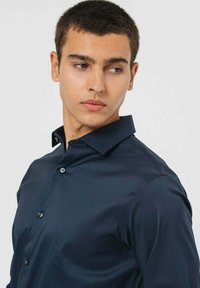 Camicia blu navy con bottoni realizzata in tessuto liscio, dotata di colletto, maniche lunghe e design aderente con bottoni a vista.