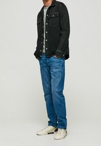 Svart jeansjacka med två bröstfickor, grå t-shirt med rund hals, blå jeans och ljusa sneakers med mörk detalj på hälen.