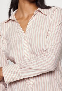 Camicia a maniche lunghe a righe rosa chiaro e bianche, con colletto a punta, pattina con bottoni e maniche con polsini e dettagli a bottoni.