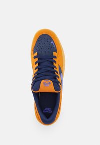Orange mockask sneaker med marinblå nätaccent, lila swoosh-logotyp, platta snören och perforerat tåområde. Gummisula för bra grepp.