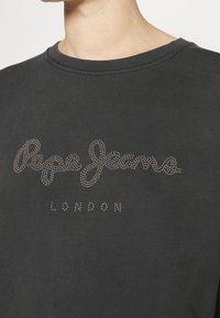 Camiseta de algodón negra con un gran logo de "Pepe Jeans" compuesto por pequeños remaches metálicos, con "LONDON" impreso debajo en una fuente sencilla.