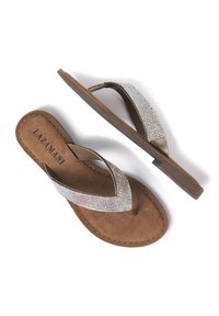 Braune Flip-Flops mit flacher Sohle. Der Riemen ist mit klaren Strasssteinen auf einer metallischen Unterlage verziert. Weiche Wildlederinnensohle mit sichtbaren Nähten.