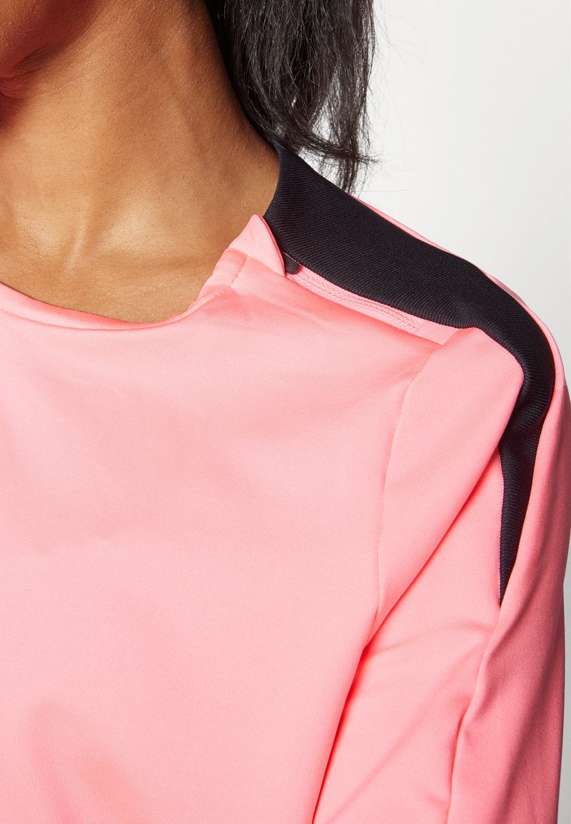 Haut rose à manches courtes avec un col rond. Présente un accent noir sur l'épaule. Fabriqué en tissu lisse et léger avec un léger brillant.