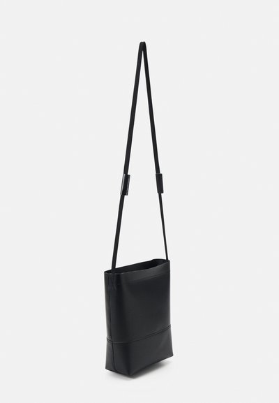 Sac croisé noir et carré en cuir lisse, avec une bandoulière ajustable et un design à ouverture supérieure. Style minimaliste sans matériel visible.