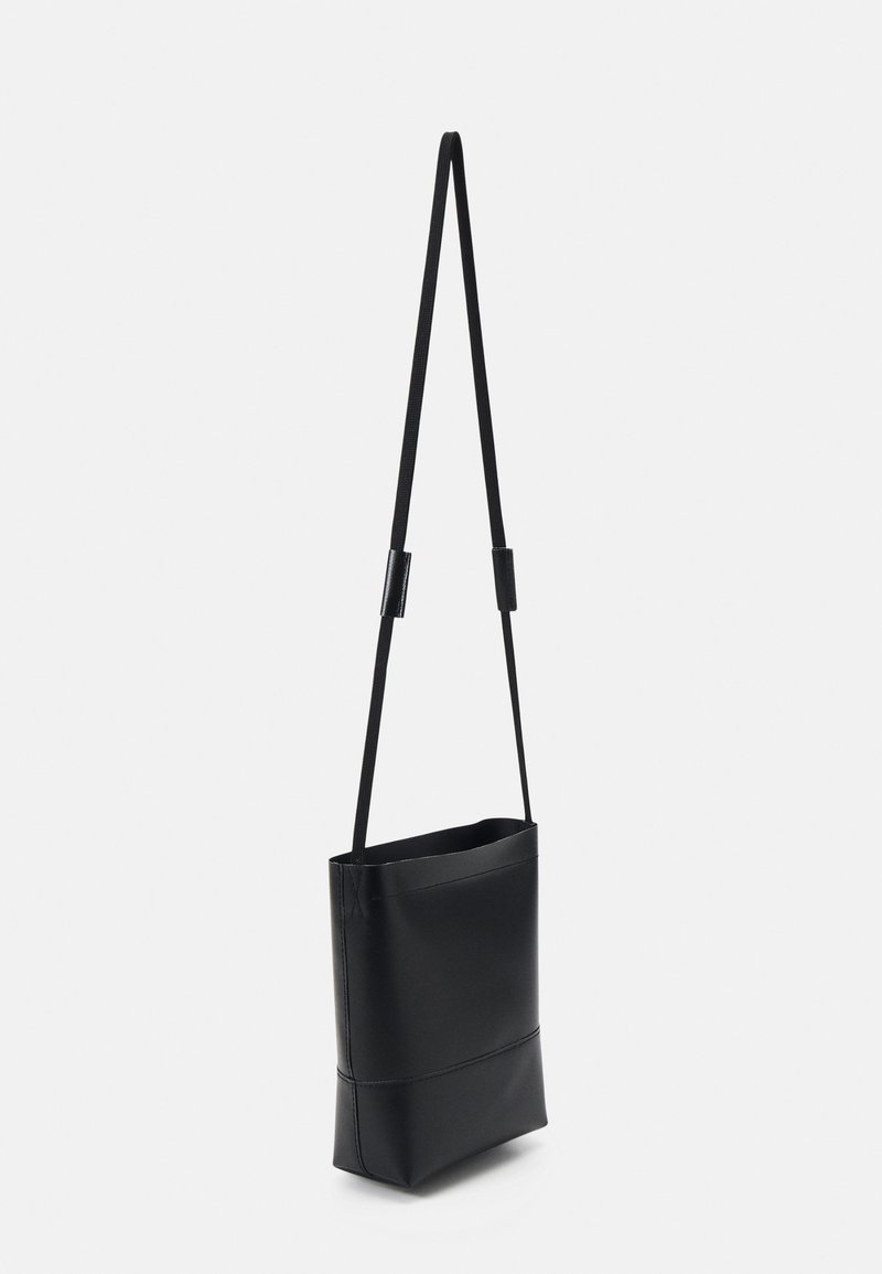 Borsa a tracolla nera e quadrata con esterno in pelle liscia, tracolla regolabile e design a cima aperta. Stile minimalista senza hardware visibile.