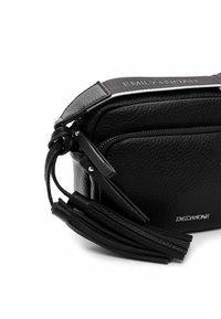 Černá kožená crossbody taška s texturovaným povrchem, obsahující kapsu na zip, detaily s třásněmi a značkový nastavovací popruh.