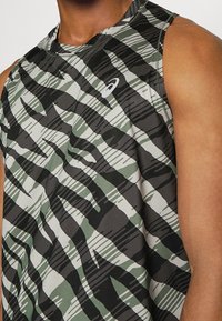 Bezramenný sportovní tank top v maskáčovém vzoru se zelenou, černou a bílou. Vyrobeno z lehké tkaniny s kulatým výstřihem a akcentem loga.