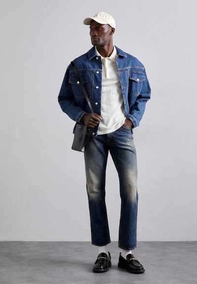 Denim dzseki elülső zsebekkel, világoskék ing, elhalványult kék farmernadrág és fekete loaferek. Fehér sapka és keresztbody táska teszi teljessé a megjelenést.