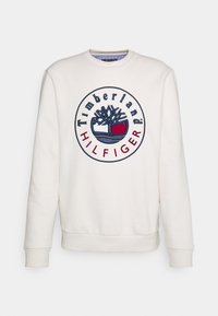 Felpa bianca con logo ricamato rotondo raffigurante un albero e dettagli colorati in rosso, blu e bianco. Tessuto morbido, design con scollatura a girocollo.