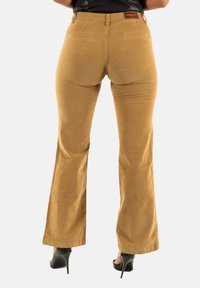 Pantalones de pana de campana en un cálido color caramelo, con una cinturilla, dos bolsillos traseros y una textura suave.