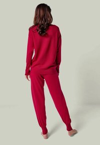 Roter Strick-Loungewear-Set mit lockerer Passform, langärmligem Oberteil und passenden Hosen mit gerafften Bündchen. Sanfte Textur, minimale Details.