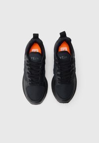 Ζευγάρι μαύρων sneakers VEJA με κορδόνια και φωτεινές πορτοκαλί σόλες, ορατό από πάνω σε λευκό φόντο.