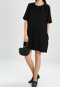 Robe noire à manches courtes, à coupe ample, avec un col rond et des poches latérales. Associée à un petit sac à main noir et des ballerines.