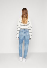 Vit kortärmad tröja med svarta ränder, ihop med ljusblå högmidjade jeans och vita sneakers, sedd bakifrån.