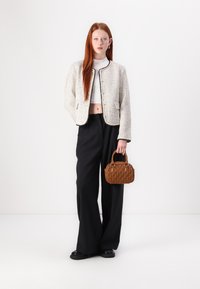 Tweed jacket in cream with black trim, cropped fit; wide black trousers; quilted brown handbag with dual handles; smooth black shoes.
