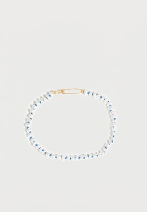 Bracelet délicat avec de petites perles blanches enfilées sur un fil bleu et sécurisé par un fermoir en or, présenté sur un fond blanc.