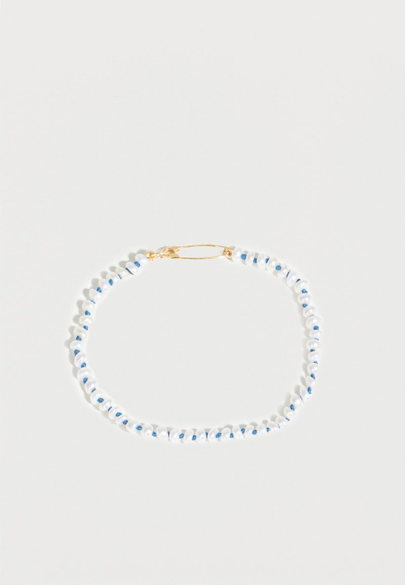 Λεπτό βραχιόλι με μικρές λευκές χάντρες περασμένες σε μπλε κορδόνι και σταθεροποιημένο με χρυσό κούμπωμα, παρουσιασμένο σε λευκό φόντο.