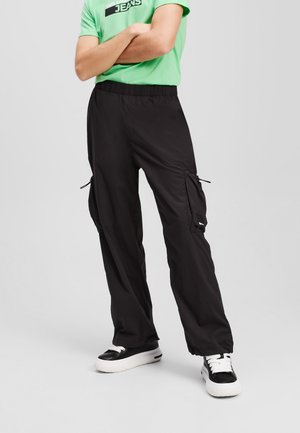 Black cargo pants with a relaxed fit, featuring zippered pockets, elastic waistband, and adjustable cuffs, paired with a green t-shirt.