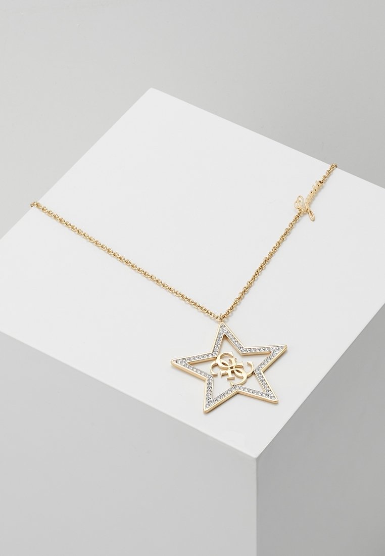 Collier chaîne en or avec un pendentif en forme d'étoile orné de petits cristaux et un logo entrelacé à l'intérieur, présenté sur une surface blanche.