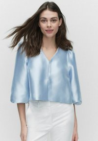 Avskuren blå satinblus med V-ringning och trekvartslånga ärmar, med en slät, glansig textur och minimal sömdetaljering.