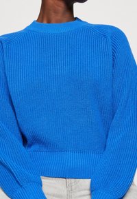 Niebieski sweter z dzianiny z teksturowanym ribbingiem, okrągłym dekoltem i długimi rękawami. Tkanina ma jednolity wzór i elastyczny dół.