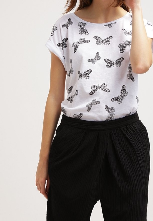 Camiseta blanca de manga corta con un patrón de mariposas en negro. Combinada con pantalones negros con textura y plisados.