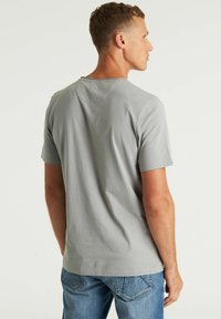 Lichtgrijs katoenen t-shirt met korte mouwen, ronde hals en een subtiele gestikte detail op de achterkant. Gepaard met blauwe denim jeans.