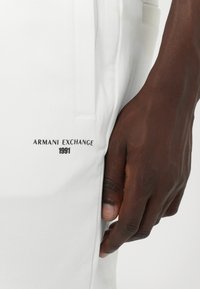 Witte broek met een gladde textuur, voorzien van een zwart "Armani Exchange 1991" logo, zijzakken en een minimalistisch ontwerp.