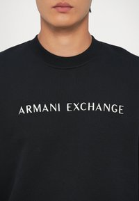 Zwarte sweatshirt van textuurstof; heeft "ARMANI EXCHANGE" geborduurd in het wit over de borst; ronde halsontwerp.