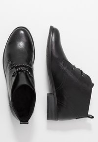 Bottines noires en cuir synthétique texturé, avec un petit talon, un détail tressé et une finition lisse. Une languette de traction sur le côté incluse.