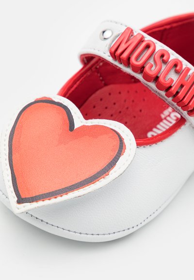 White leather shoe with a large red heart design on the toe. Features a red "MOSCHINO" strap and a textured red interior.