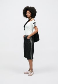 Λευκό πουκάμισο με κοντά μανίκια και μαύρες ρίγες, μαύρα βερμούδα τζιν με λευκές πλευρικές ρίγες και ανοιχτό ροζ παπούτσια με κορδόνια, με μαύρη τσάντα.