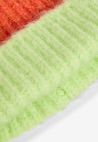 Šála z pletené tkaniny s elegantně se střídajícími živými sekcemi nadýchané oranžové a pastelově zelené barvy, s ribovanou texturou a jemným povrchem.