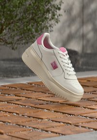 Λευκό δερμάτινο αθλητικό παπούτσι με ροζ λεπτομέρειες, παχύ πέλμα, στρογγυλεμένη μύτη και διακοσμητικές οπές. Διαθέτει λογότυπο στη πλευρά και υφασμένο πέλμα.